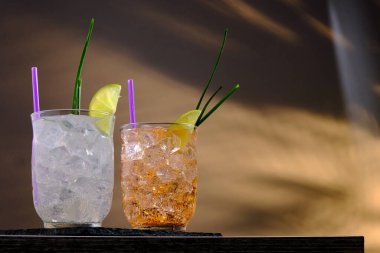 Limonlu taze kokteyller ve gri ve turuncu arka planda buzlu camlar. Yaz aylarında alkolsüz içecekler, içecekler ve kokteyller. Boşluğu kopyala.