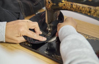 Dikiş işleminin yakın görüntüsü. Klasik dikiş makinesiyle dikiş atan bir kadın eli. Seçici odak.