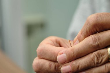 Dikiş ipliği iğnesine iplik geçirmeye çalışan kadın ellerinin yakın çekimi. Seçici odak,