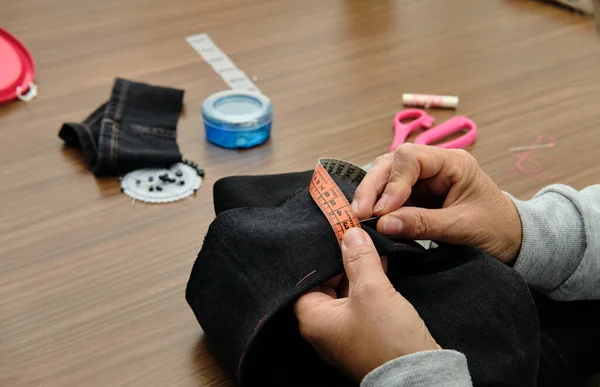 Close-up of female hands sewing fabric with needle and measuring tape at seamstress workplace.