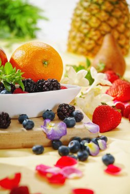 Kahvaltı brunch tablo taze ve güneş sabah, çiçek, gül, viyola, pembe çilek, portakal, yaban mersini, böğürtlen, mango, ahududu, beyaz masa örtüsü, beyaz kase ve çiçekler.