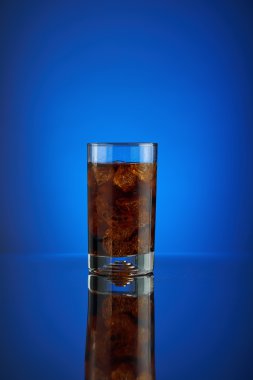 Splash cam kola meşrubat mavi bir arka plan üzerinde yenileniyor. Soğuk sıvı İçecek coca buz ile soğuk bir bardak içine. Restoran ve bar teşvik için içecek. Köpüklü izole Closeup dizayn kahverengi likör.