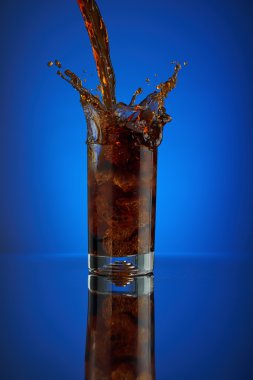 Splash cam kola meşrubat mavi bir arka plan üzerinde yenileniyor. Soğuk sıvı İçecek coca buz ile soğuk bir bardak içine. Restoran ve bar teşvik için içecek. Köpüklü izole Closeup dizayn kahverengi likör.