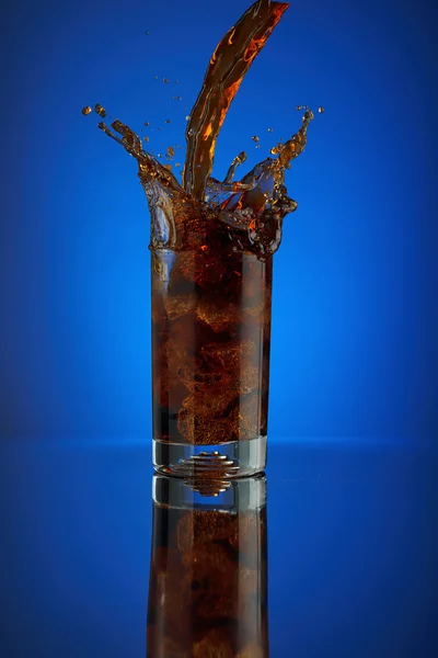 Rafraîchissant verre éclaboussure cola boisson gazeuse sur un fond bleu. Laisser refroidir la coca liquide dans un verre froid avec de la glace. Boisson pour promouvoir le restaurant et le bar. Gros plan isolé design liqueur brune pétillante . — Photo