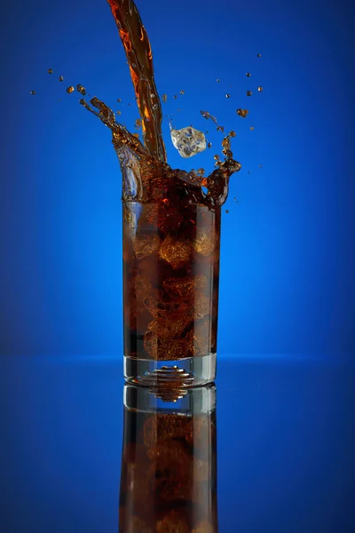 Rafraîchissant verre éclaboussure cola boisson gazeuse sur un fond bleu. Laisser refroidir la coca liquide dans un verre froid avec de la glace. Boisson pour promouvoir le restaurant et le bar. Gros plan isolé design liqueur brune pétillante . — Photo