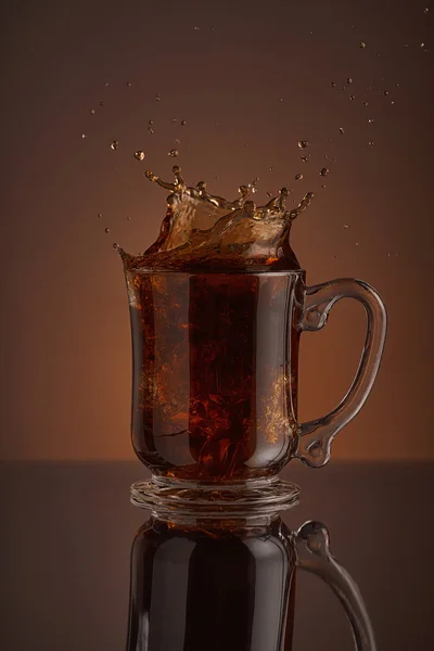 Splash black ice coffee drink on brown background. Refreshing splash of black ice coffee drink on a brown background. Liquid drink pouring into a cup with ice. Pour high speed beverage for promoting restaurant, bistro and bar. Close-up design liquor — Stock Photo, Image