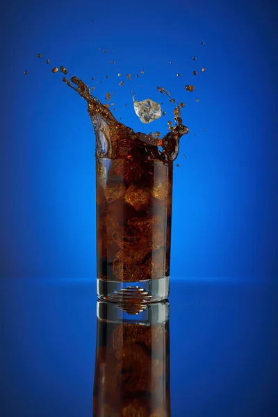 Uppfriskande splash glas cola läsk på en blå bakgrund. Kall flytande dryck coca i ett kallt glas med is. Dryck för att främja restaurang och bar. Närbild isolerade design brun sprit mousserande. Stockbild