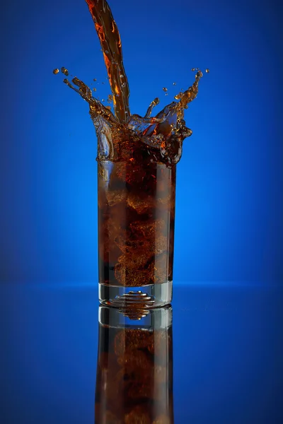 Uppfriskande splash glas cola läsk på en blå bakgrund. Kall flytande dryck coca i ett kallt glas med is. Dryck för att främja restaurang och bar. Närbild isolerade design brun sprit mousserande. Stockfoto