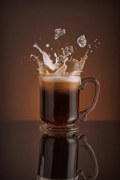 Splash de bebida de café gelado em um fundo marrom. refrescante Gced cappuccino bebida líquida derramando em uma caneca, xícara com cubos de gelo. Onda de bebidas frias. Desenho de close-up leite licor, café e gelo . — Fotografia de Stock