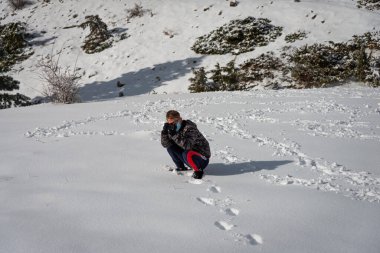 Genç adam karla kaplı bir arazide fotoğraf çekiyor, hobi ya da boş zaman aktivitesi.