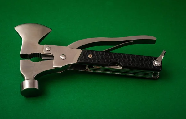 camping or survival multi tool , with axe hammer and pliers on green background .