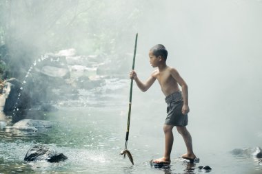 Çocuk nehirde balık tutuyor.