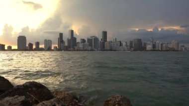 Miami şehir merkezinin arkasında güneş batıyor Biscayne Körfezi önplanda ve dalgalar akıyor
