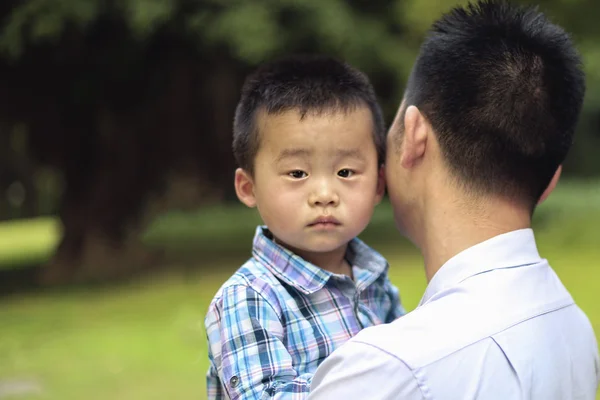 Chinese dad hugging his little son. Boy looking ahead. Dad and son walking in the park.