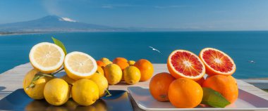 Mavi denizli ahşap bir masada portakal ve limon kes ve arka planda Etna Dağı olsun.