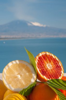 Mavi denizli ahşap bir masada portakal ve limon kes ve arka planda Etna Dağı olsun.
