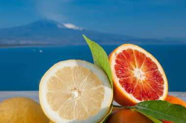 Mavi denizli ahşap bir masada portakal ve limon kes ve arka planda Etna Dağı olsun.