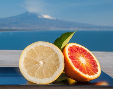 Mavi denizli ahşap bir masada portakal ve limon kes ve arka planda Etna Dağı olsun.