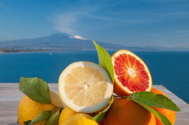 Mavi denizli ahşap bir masada portakal ve limon kes ve arka planda Etna Dağı olsun.