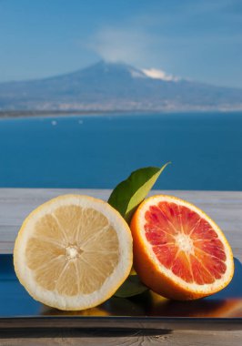 Mavi denizli ahşap bir masada portakal ve limon kes ve arka planda Etna Dağı olsun.