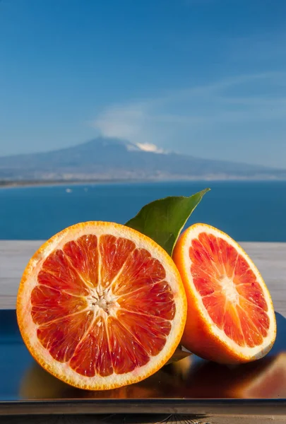 在蓝海和埃特纳山为背景的木制桌子上切橙子 图库照片