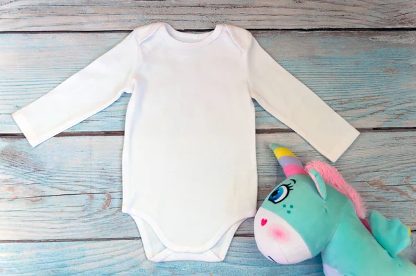 Tahta arka planda uzun kollu beyaz bir bebek tulumu. Harfler ya da metinleriniz için boşluk kopyalayın. Düz yatış modeli. Stok fotoğrafı. Biçimli stok fotoğrafçılığı.