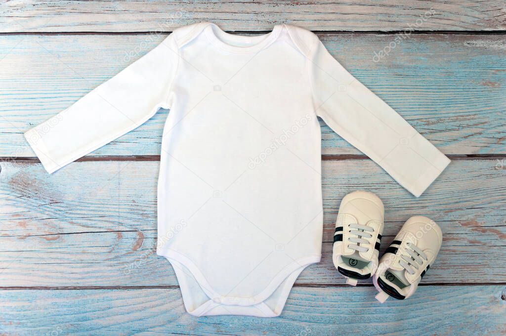 Top view white baby bodysuit with long sleeve on wooden background. Copy space for lettering or your text. Flat lay mockup. Stock photo. Styled stock photography.