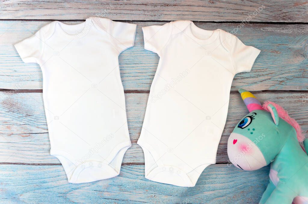 Layout Flat Put on a two white baby bodysuit on a wooden background with unicorn toy. Layout for design and placement of logos, advertising. Styled stock photography, stock photo. flat lay.