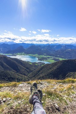 Yüksek bir dağda oturan gezgin bacakları. Özgürlüğe yolculuk konsepti. Güzel bir manzaraya karşı botları gezdirmek. Nefes kesici dağ manzarası. Yaz tatili macera sahnesi.