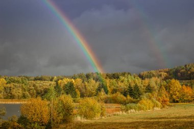 Kırsalda çifte gökkuşağı. Yağmurlu bir günde güzel yoğun gökkuşağı renkleri. Hava tahmini. Koyu dramatik gökyüzü üzerine gökkuşağı düşmüş kırsal alan. Özgürlük mutluluk kavramı.