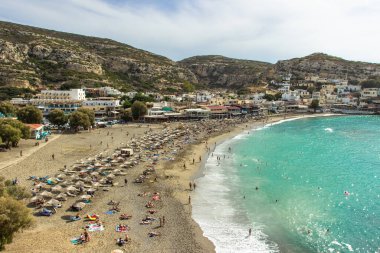 Matala, Girit - 8 Ekim 2019. Yunanistan 'ın Matala plajındaki panorama, açık deniz, kumlu sahil ve dinlendirici insanlar. Sakin yaz atmosferi. Ünlü turistik yer. Tatil gezisi konsepti.