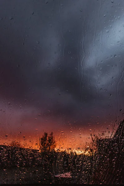 Drops on glass in rainy day. Rain outside window in autumn day. Texture of raindrops, wet glass. Rainy window background. View through the window in a rainy day at a colorful sunset. Staying at home