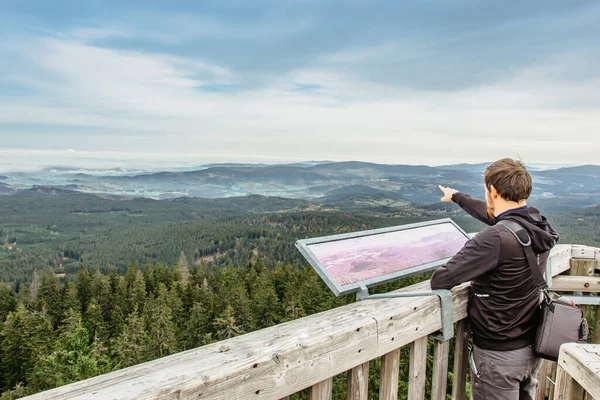 Man on observation tower looking in a map.Male backpacker enjoying view of misty landscape.Man Traveler on Czech Boubin mountain summit.Travel Lifestyle success leisure concept.Active vacation outdoor