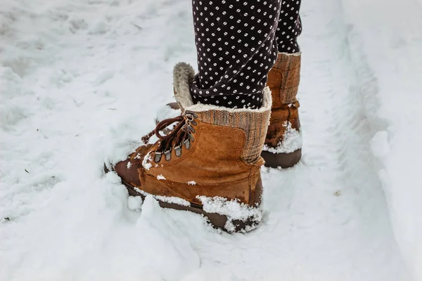 Detail of warm winter boots in snow.Female feet in brown shoes, winter walking in snow.Low angle view of standing female legs with snowy boots. Winter scenic background copy space.Pair of shoes