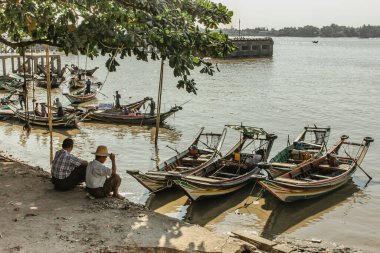 Yangon, Myanmar - 19 Ocak 2020. Nehrin kıyısında oturan balıkçılar. Yangon 'daki yoğun nehir limanı. Balıkçı tekneleri ve Asya yaşam tarzı. İki eski dost konuşuyor ve dünyayı izliyorlar.