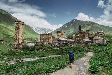 Happy male traveller in Ushguli,UNESCO site,Georgia.Backpacker exploring the Greater Caucasus mountains.Rural stone houses,village life,wild pure nature.Popular travel destination.Wanderlust man clipart