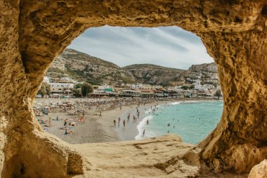 Matala, Girit - 8 Ekim 2019. Yunanistan 'ın Matala plajı ve mağaralarının panoraması, masmavi suları, kumlu plajları ve dinlendirici insanları ile. Sakin yaz atmosferi. Ünlü turistik mekan. Tatil seyahati kavramı.