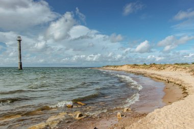 Baltık Denizi kıyısında güneşli bir yaz günü.Wandelust geçmişe yolculuk. Su enerjisinin gücü geçiyor. Eski deniz feneri, dalgalar ve çakıllı kumsal manzaralı soğuk deniz manzarası.