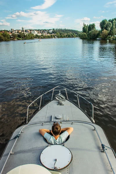 Happy young man relaxing on boat floating in calm river water. Good sunny summer day in nature. Concept vacation on lake.Man enjoying view of landscape city in background. Going to adventurous holiday