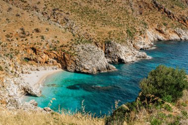Sicilya, İtalya 'da plaj tatili, turkuaz su, Zingaro Doğa Koruma Alanındaki boş kumlu plaj. Tatil cenneti seyahat manzarası. Kayalarla dolu kıyı şeridi. Alışveriş merkezi mavi lagünü, berrak su, berrak yüzme..