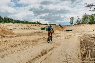 Bisikletçi, kum taşı ocağında bisiklet sürüyor. Port, eğlence ve boş zaman. Spor kıyafetleri ve dağ bisikleti üzerindeki yeşil başlıklı aktif sakallı adam.