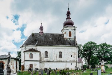 Puste Zibridovice, Çek Cumhuriyeti - 12 Temmuz 2021. Jeseniky dağlarındaki küçük Çek köyünde çan kulesi ve mezarlığı olan eski beyaz barok Saint Mary Kilisesi. Kültür Mirası..