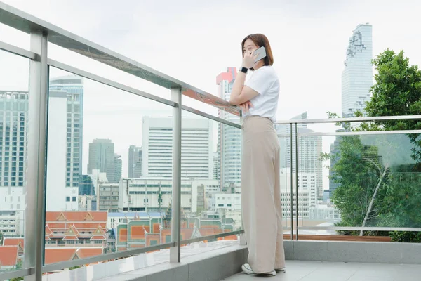 solo asian woman during use phone and relax at rooftop with city background