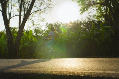 Siluet Asyalı kadın ilkbaharda ağacın altında bisiklet sürüyor.
