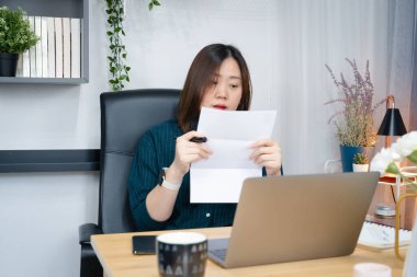 Asyalı kadın vergisini kontrol ediyor ve bilgisayarını evden geri ödeme için kullanıyor.