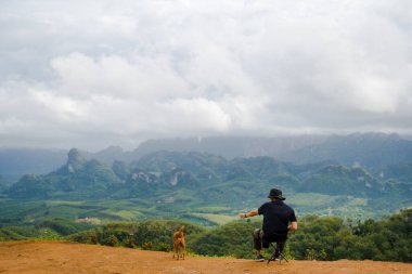 Tek başına yürüyüş yapan adam köpeğiyle dağın tepesinde rahatlar.
