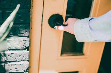 Kadın eli kot kumaşlı açık ahşap kapı tokmağına dokunuyor.