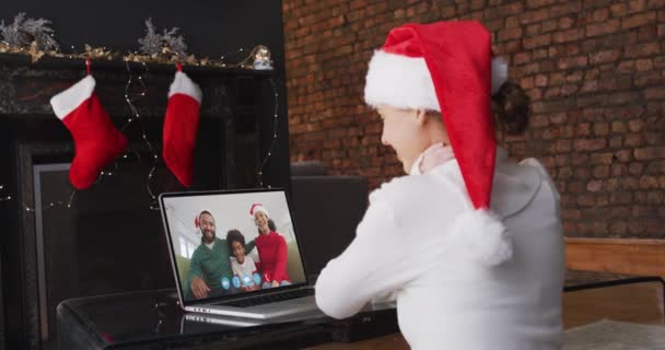 白种人女人呆在家里戴着桑塔帽 坐在壁炉边与朋友们在笔记本电脑屏幕上视频聊天 动作缓慢 大流行病期间圣诞节时的自我隔离 — 图库视频影像