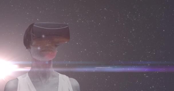 Kobieta nosząca zestaw słuchawkowy VR nad wszechświatem z wieloma gwiazdami i świecącą plamą światła w tle — Wideo stockowe