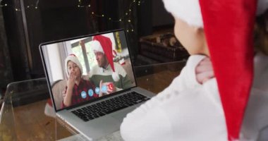 Beyaz kadın, Noel Baba şapkalı, beyaz bir adam ve oğlu ile görüntülü konuşma yapıyor. Evde, Noel Baba şapkası hediye kutusunun içinde. Koronavirüs salgını sırasında karantina karantinasına sosyal uzaklık